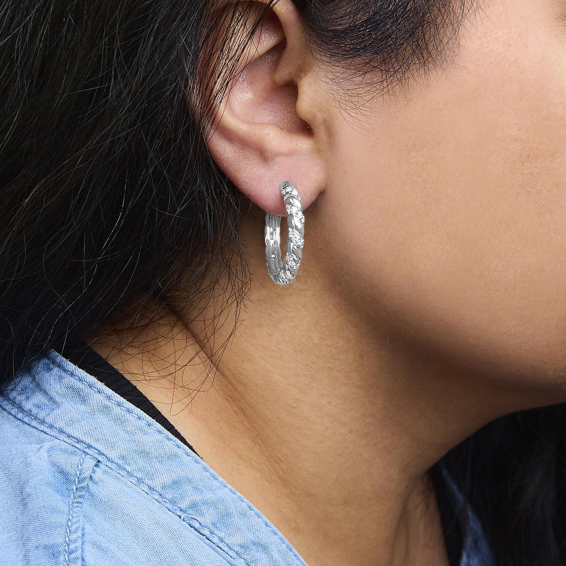 Close-up side view of a model wearing white metal hoop earrings adorned with round white gemstones in prong settings.