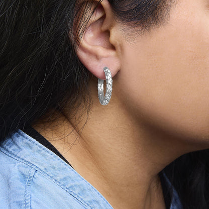 Close-up side view of a model wearing white metal hoop earrings adorned with round white gemstones in prong settings.