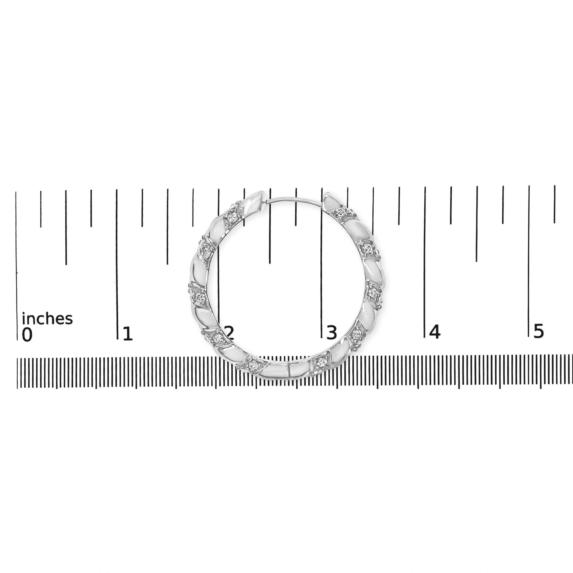 White metal hoop earring with alternating smooth and textured segments featuring round prong-set white gemstones, photographed from above on a ruler for size reference.