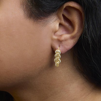 Close-up side view of a yellow metal earring with linked oval shapes, each lined with small white gemstones, worn on a model.