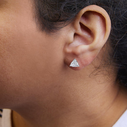 Close-up side view of a white metal earring featuring a trillion-shaped white gemstone in a 3-prong setting, worn on a model's ear.