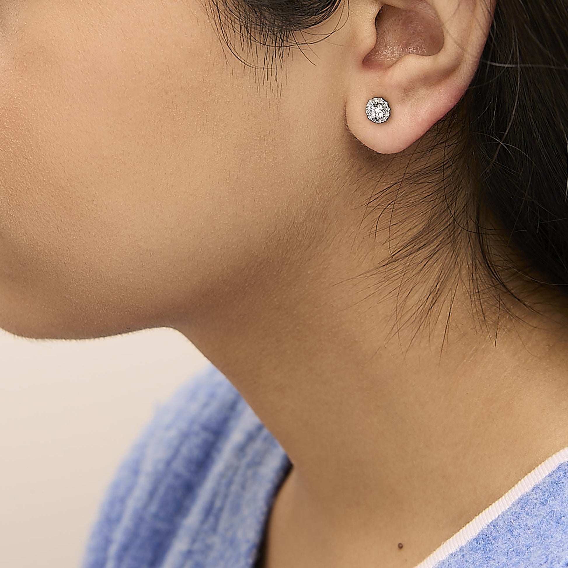 Close-up side view of a model wearing a white metal stud earring with a central round white gemstone surrounded by smaller round white gemstones.