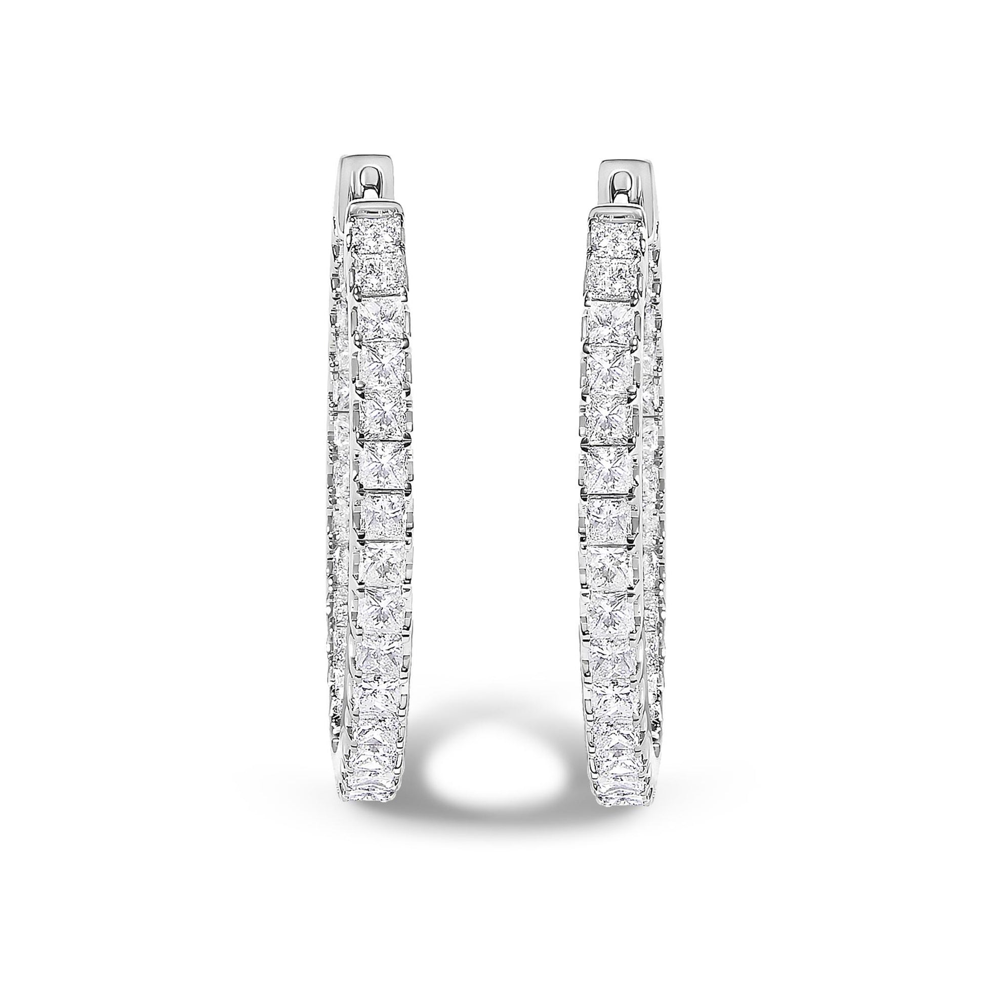 Front-facing close-up of a pair of white metal hoop earrings adorned with princess shaped white gemstones in a prong setting.