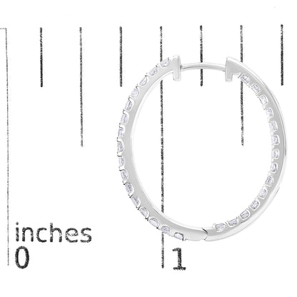 Close-up front view of a white metal hoop earring with white princess-shaped gemstones in prong settings, shown on a scale with inch markings.