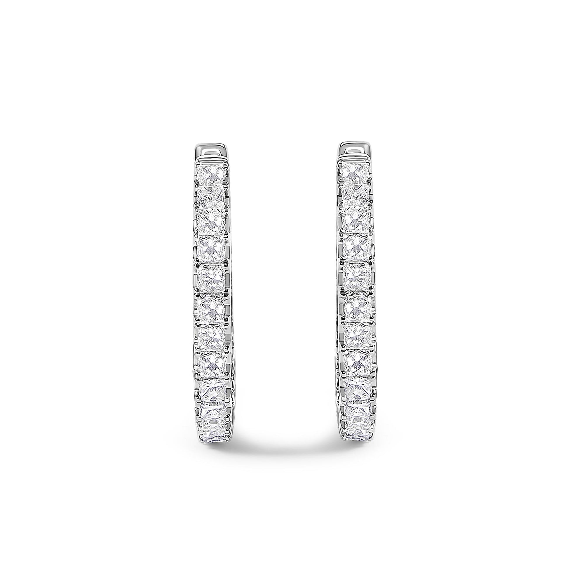 Close-up front view of a pair of white metal hoop earrings set with rows of princess-shaped white gemstones in prong settings.