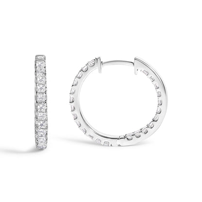 Close-up shot of a pair of white metal hoop earrings with princess-shaped white gemstones in prong settings all around the outer surface, shown against a white background.