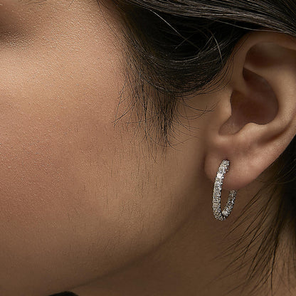 Close-up side view of white metal hoop earrings with princess-shaped white gemstones in prong setting, shown worn on a model.