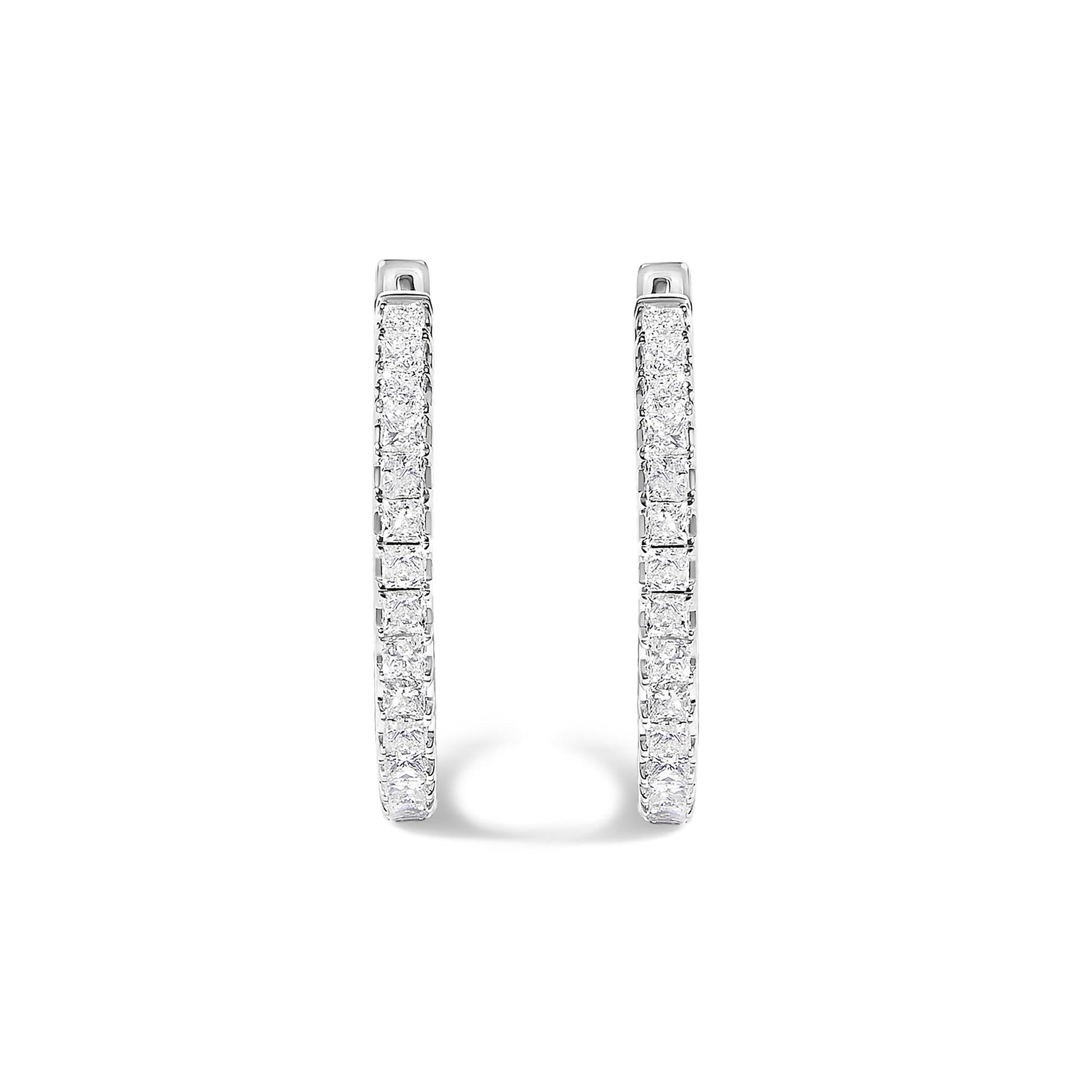Close-up front view of a pair of white metal hoop earrings featuring princess-shaped white gemstones set in prong settings along the outer curves, shown on a white background.