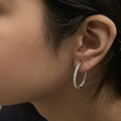 Close-up side view of a model wearing white metal hoop earrings encrusted with prong-set princess-shaped white gemstones.