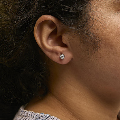 Close-up side view of a model wearing a white metal earring featuring a central white gemstone surrounded by smaller white gemstones in prong settings.