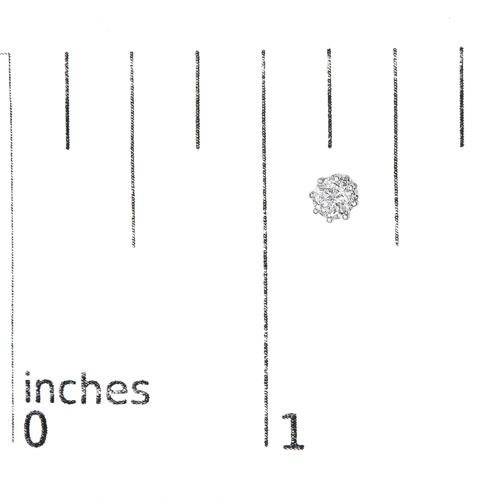 Close-up front view of a round white metal earring with clustered white gemstones, shown on a ruler for size reference.