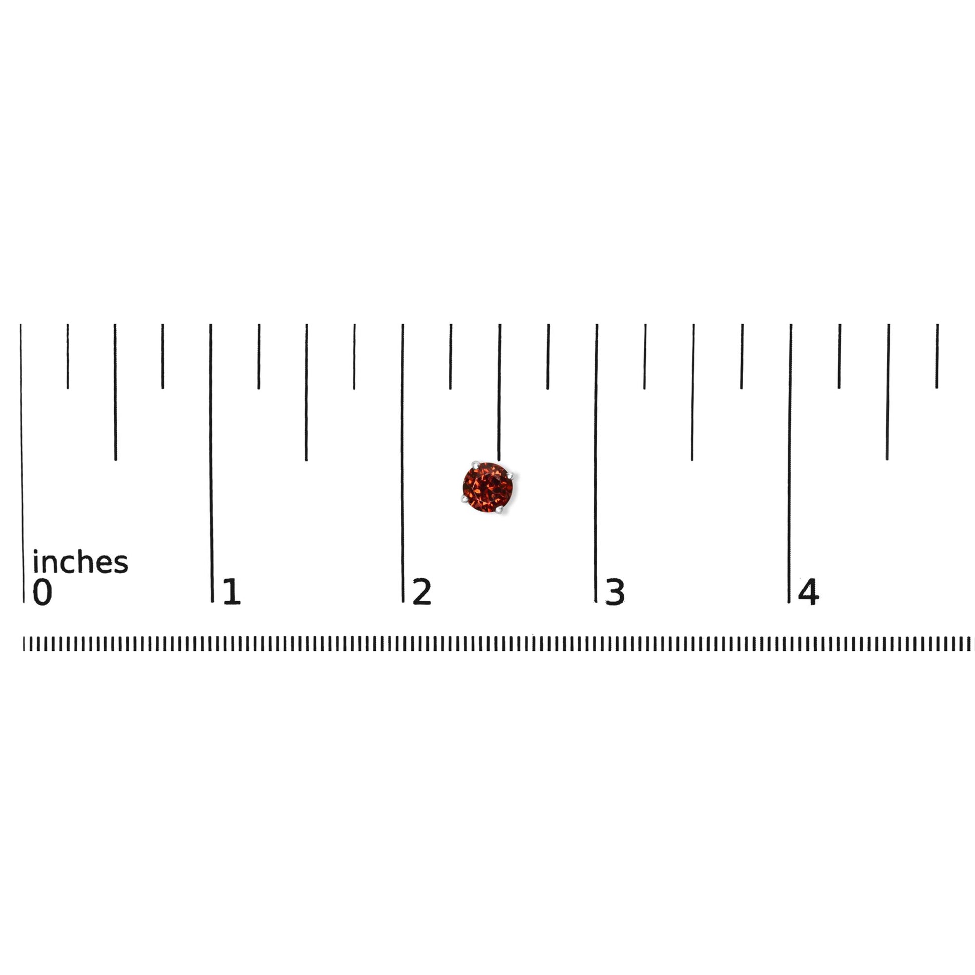 Close-up top view of a single round red gemstone earring in a four-prong white metal setting placed on a ruler for size reference.