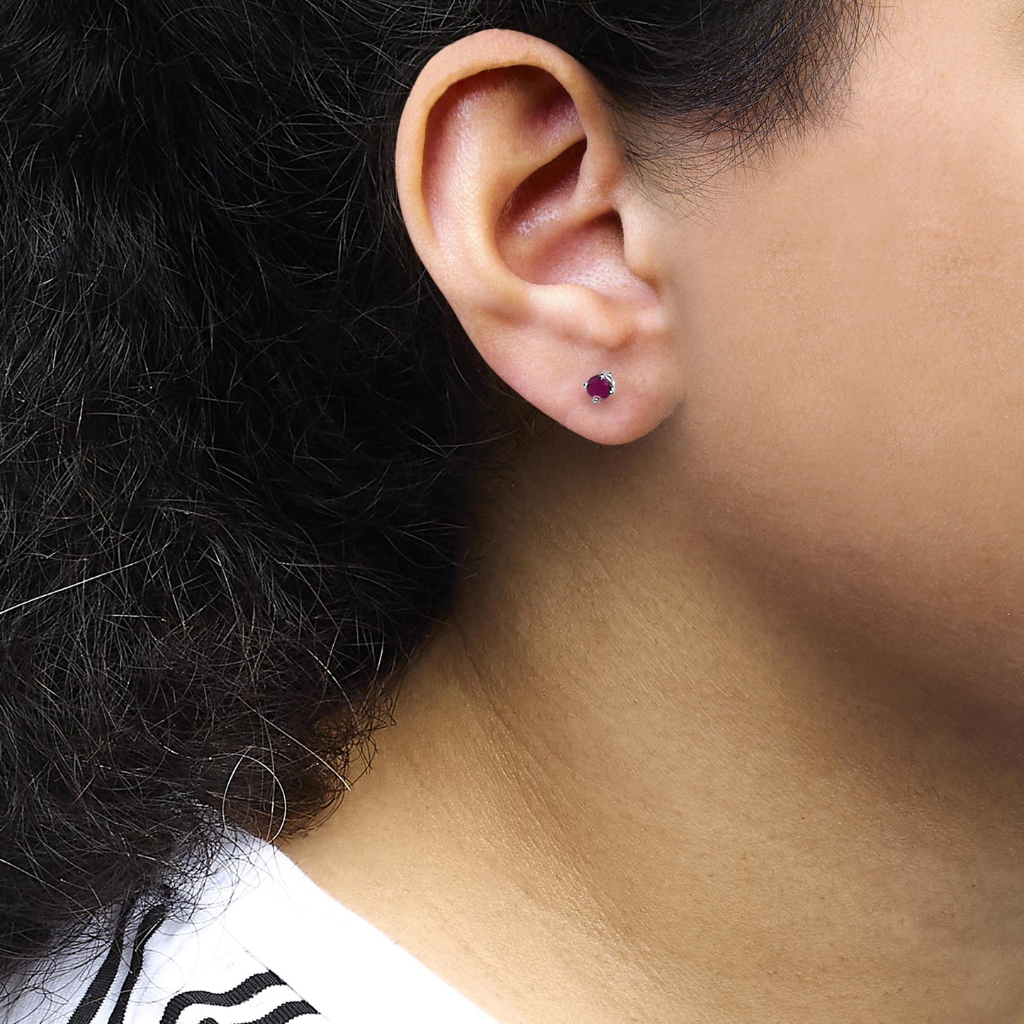 Close-up side view of a white metal stud earring with a round pink gemstone in a 4-prong setting worn on a model's ear.