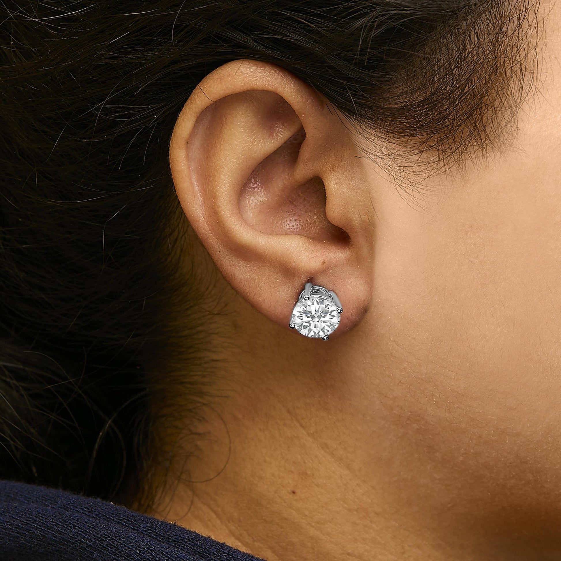 Close-up side view of a model wearing a white metal stud earring with a round white gemstone set in a four-prong setting.