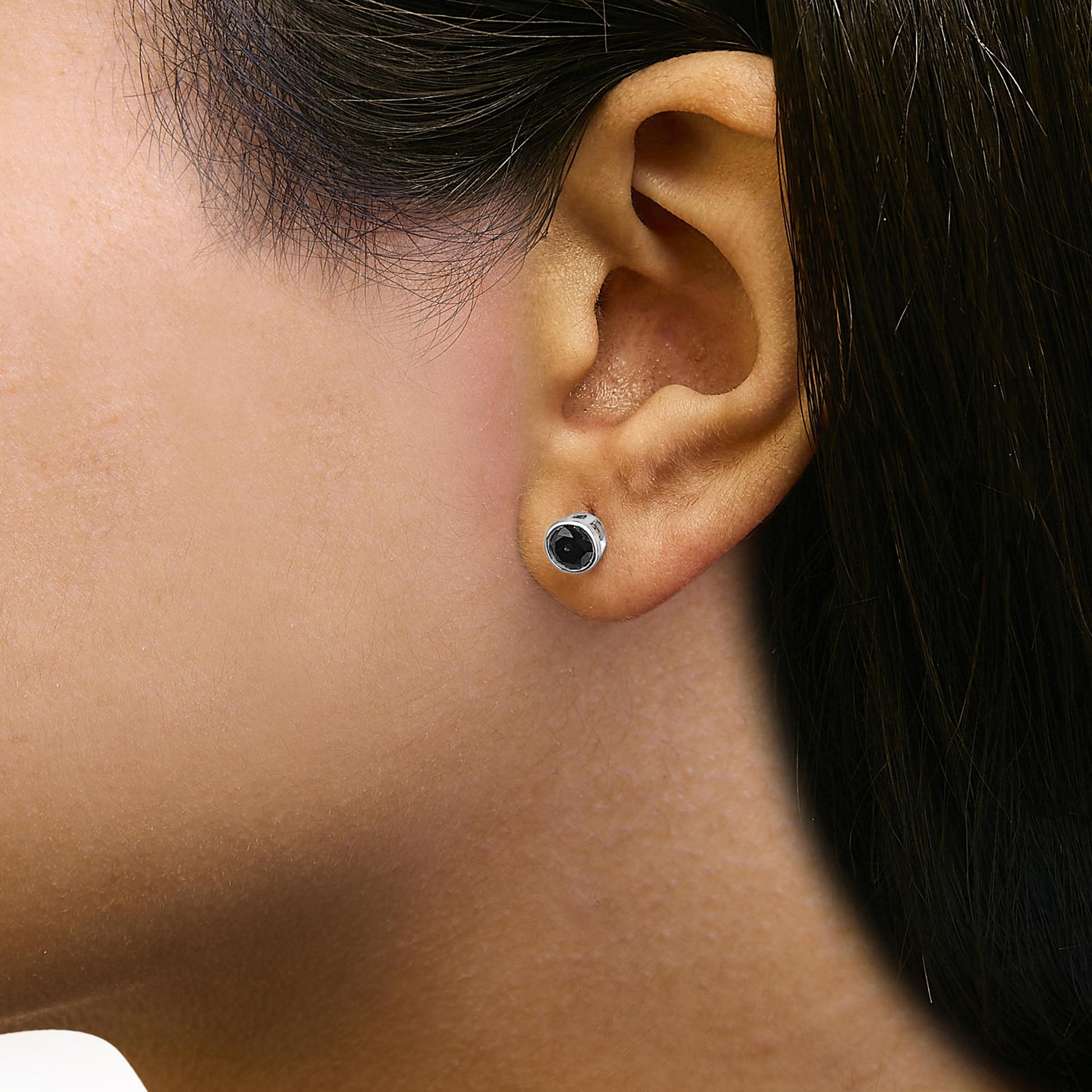 Close-up side view of a model wearing a white metal stud earring with a round black gemstone in a bezel setting.