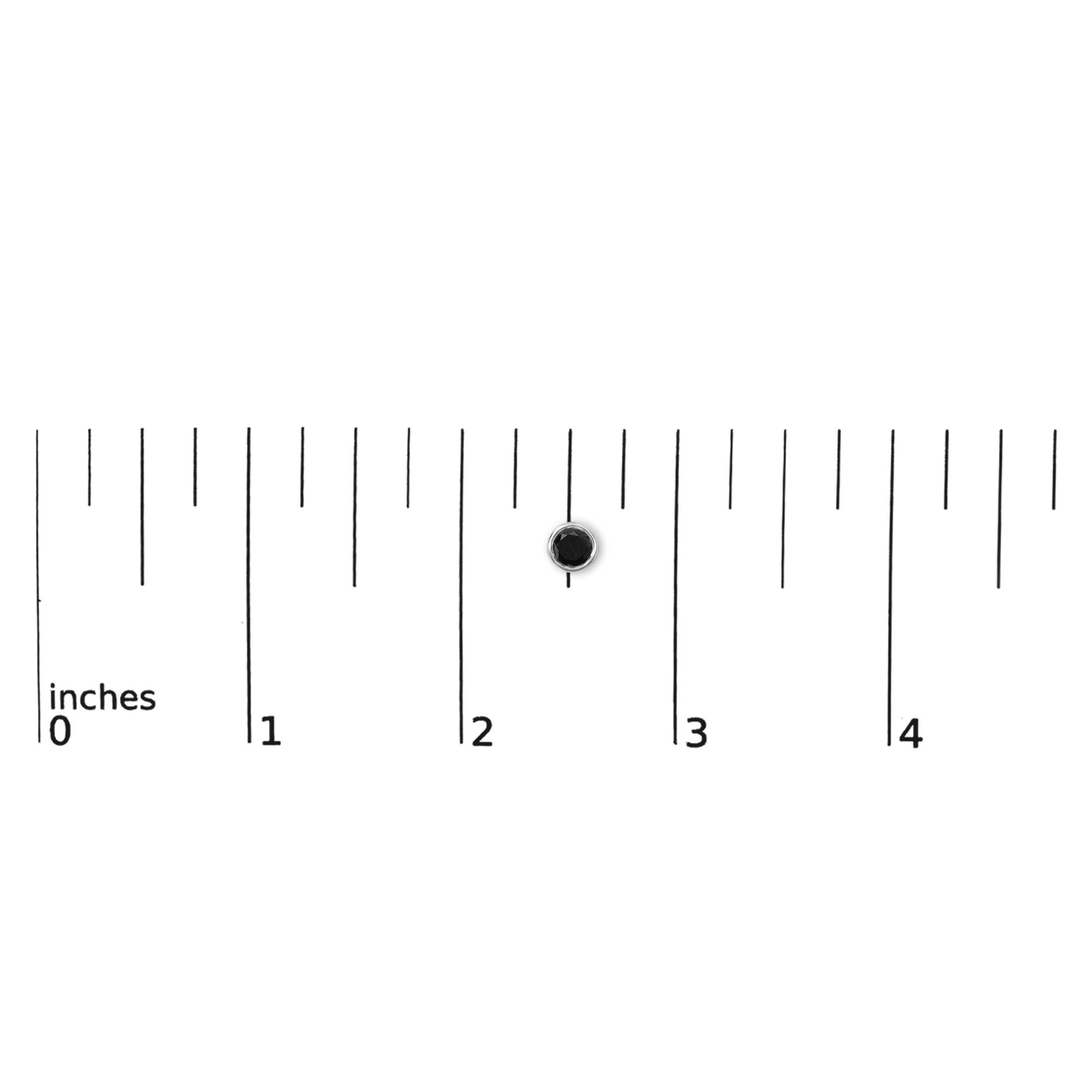 Close-up top view of small white metal stud earring with round black gemstone in bezel setting, shown on a ruler scale.