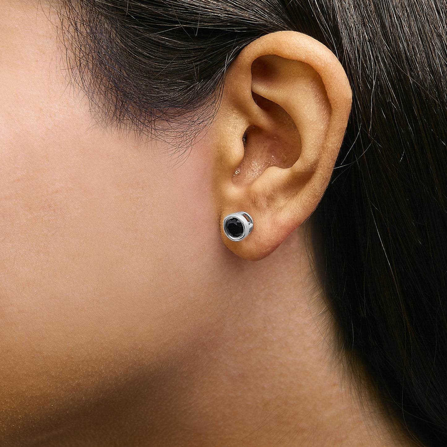 Close-up side view of a model wearing a white metal stud earring with a round black gemstone in a bezel setting.