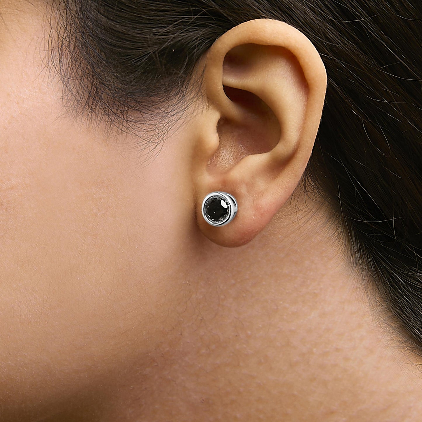 Close-up side view of white stud earring with round black gemstone in bezel setting, shown worn on a model's ear.