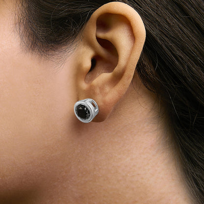 Close-up side view of a white metal stud earring with a round black gemstone in a bezel setting worn on a model's ear.