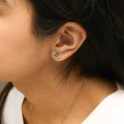 Close-up side view of a model wearing round yellow earrings featuring a circular design with white gemstones set around the edge and an infinite loop symbol in the center.