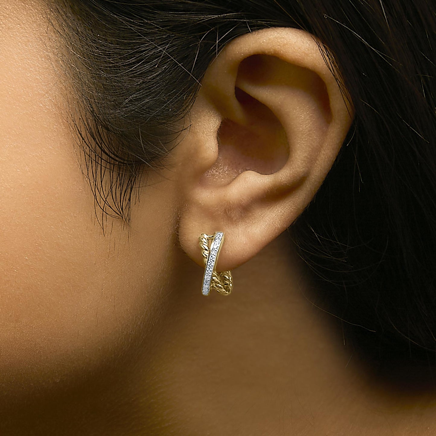 Close-up side view of a model wearing yellow metal earrings featuring a twisted design with a row of round white gemstones in prong settings.