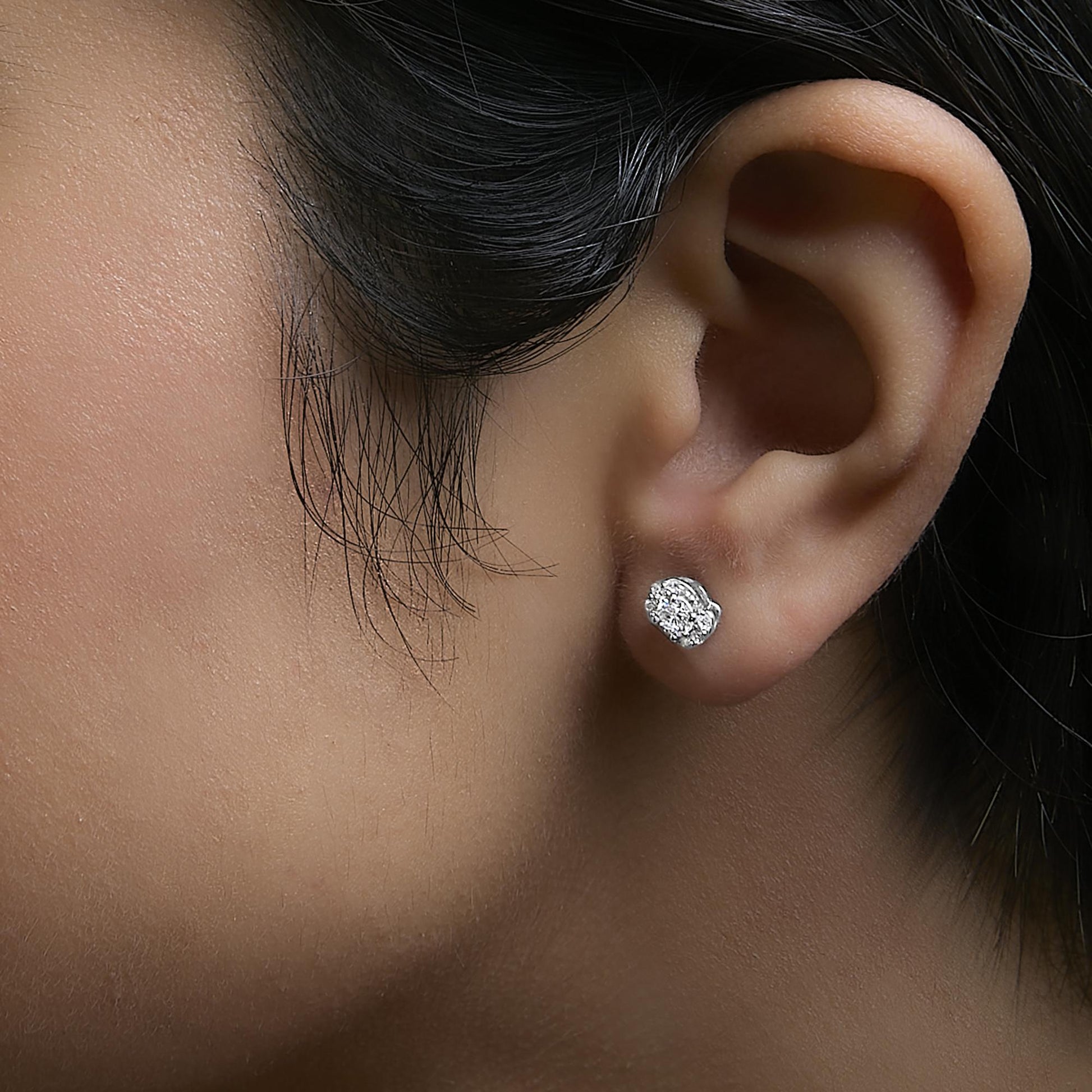 Close-up side view of a model wearing white metal stud earrings with clusters of round white gemstones in prong settings.
