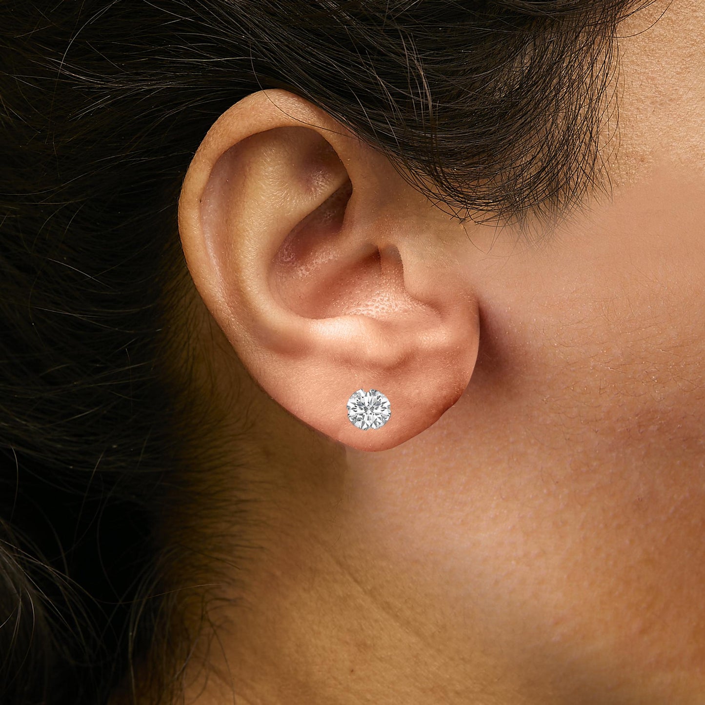 Close-up side view of a model wearing a white metal earring with a round white gemstone in a four-prong setting.