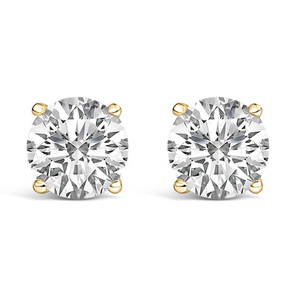 Close-up front angle of a pair of yellow metal stud earrings, each featuring a round white gemstone in a four-prong setting.