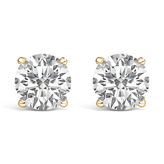 Close-up front angle of a pair of yellow metal stud earrings, each featuring a round white gemstone in a four-prong setting.