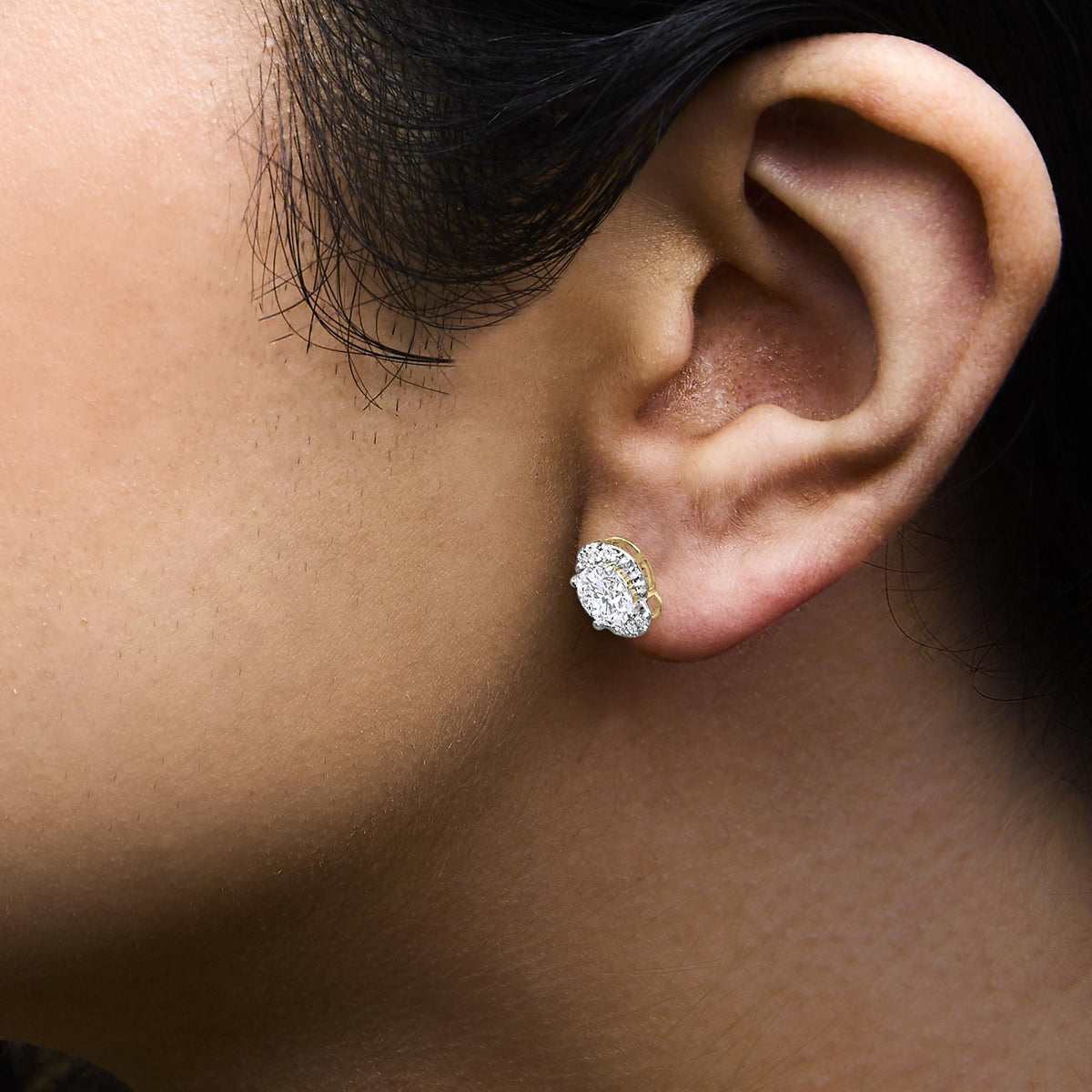 Close-up side view of a model wearing yellow metal earrings featuring multiple round white gemstones in prong settings.