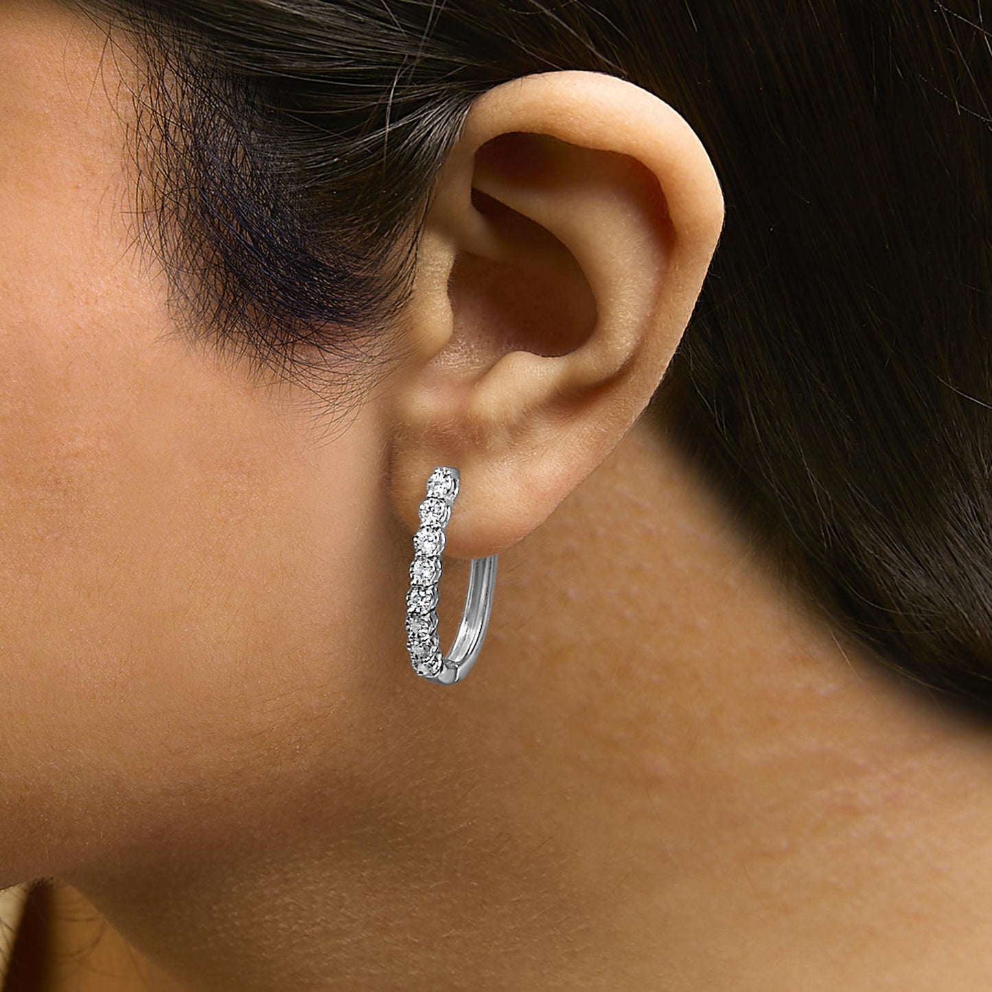 Close-up side view of a white metal hoop earring with round white gemstones set along the front, shown worn on a model.