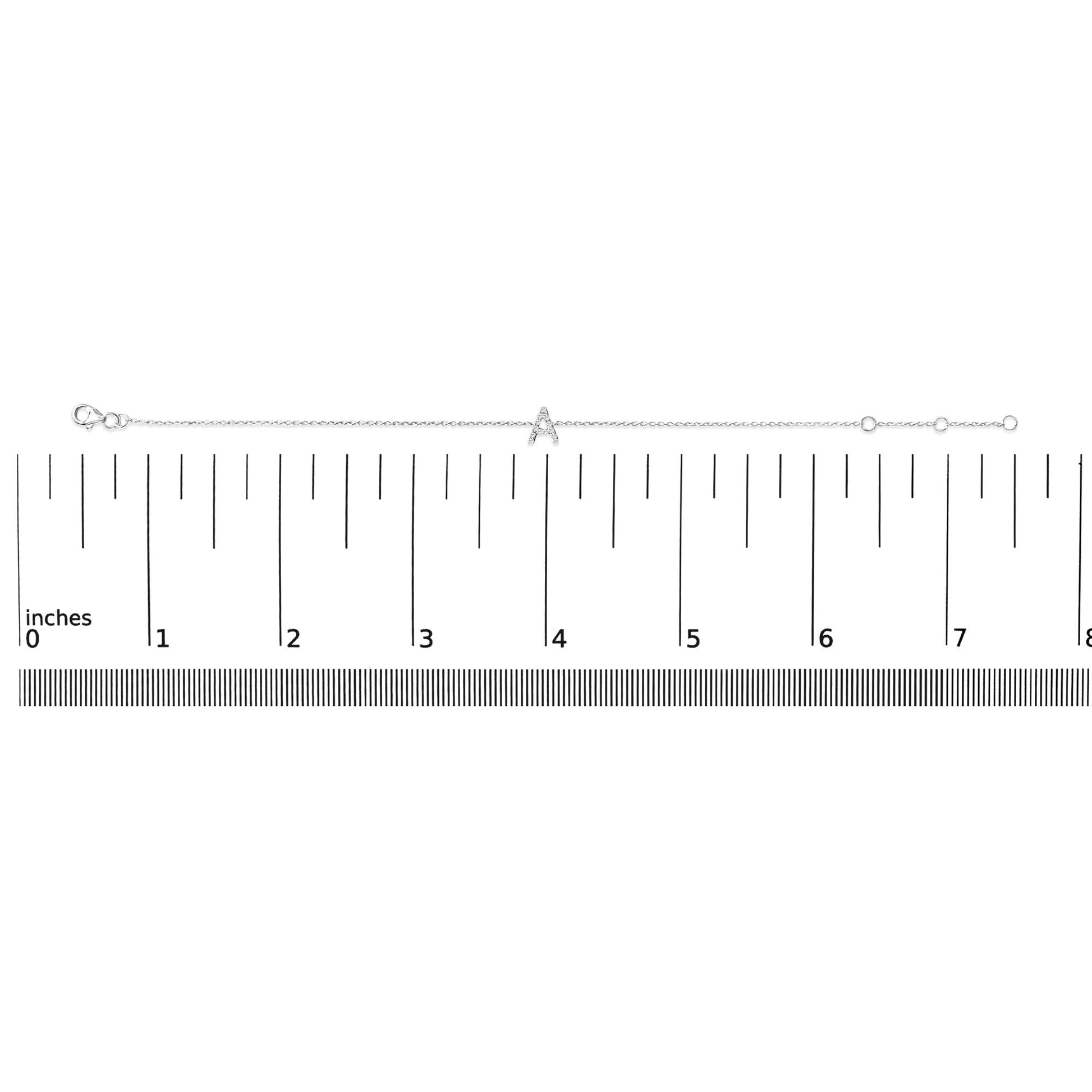 White metal bracelet with a central 'A' charm adorned with small white gemstones in a micro-pave setting, shown laid flat on a ruler for scale, image taken from a top-down angle.
