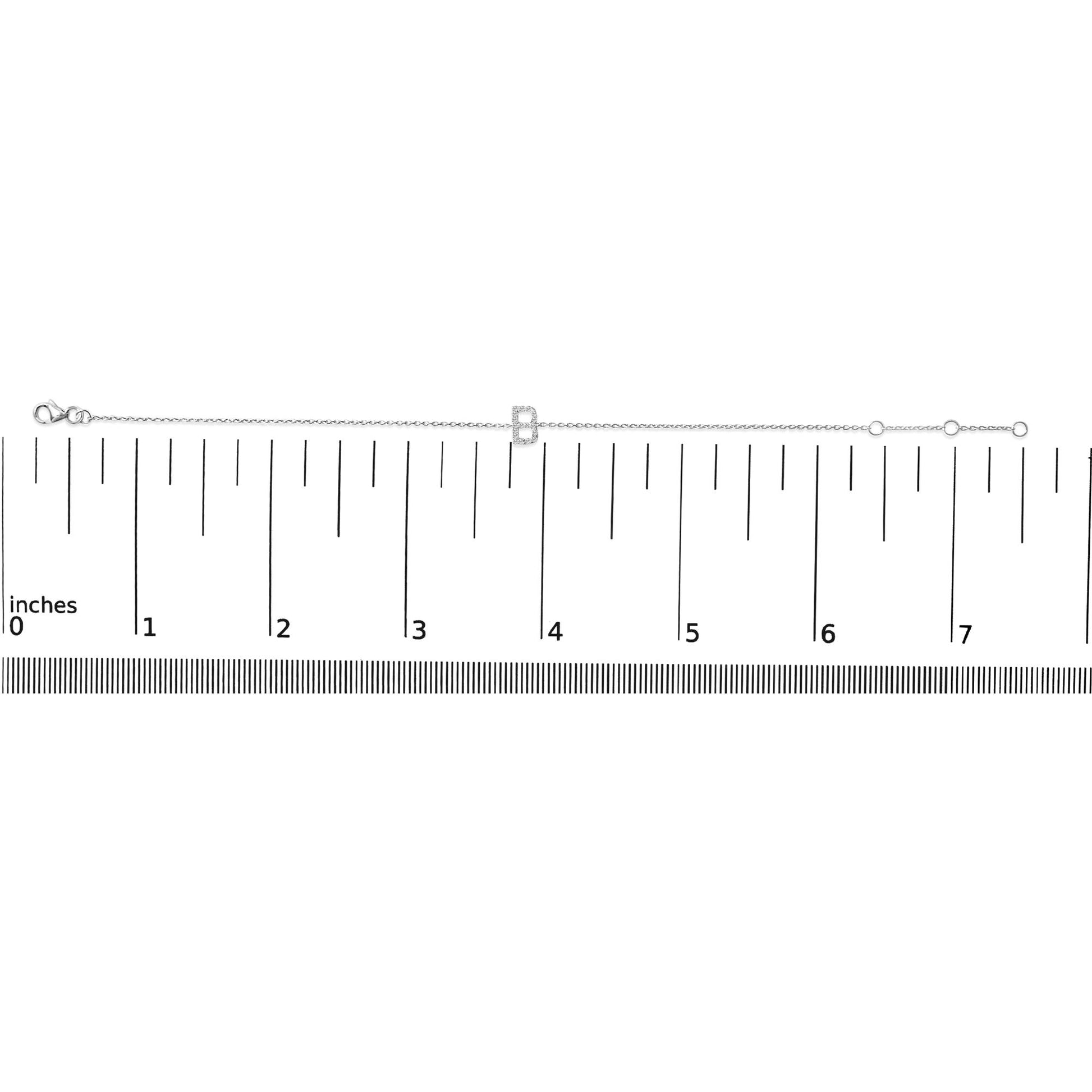 White metal bracelet with a letter-shaped charm set with white round gemstones in micro-pave setting, shown flat on a ruler scale from a top-down angle.