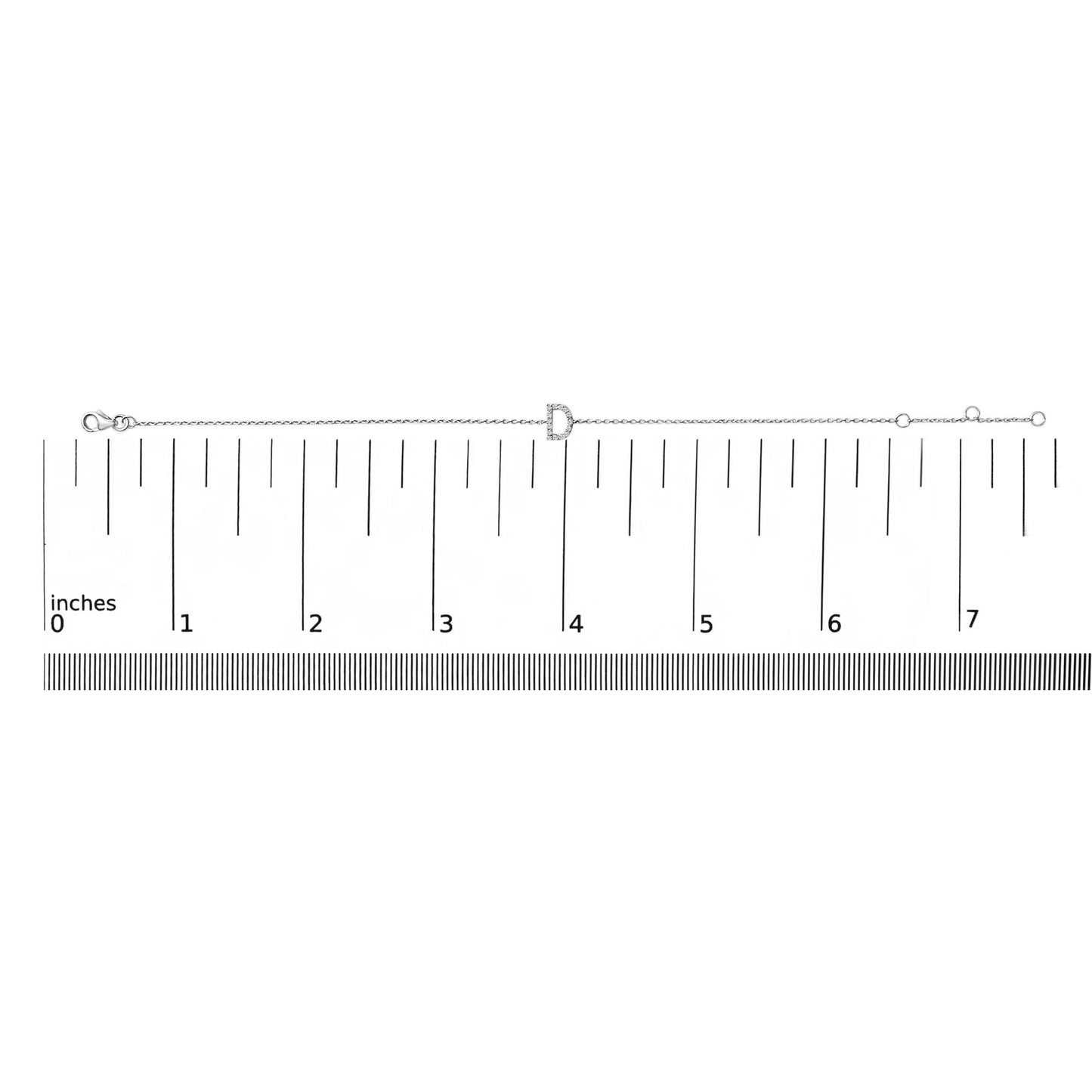 White metal bracelet with a central letter-shaped charm featuring small white gemstones in a micro-pave setting, shown laid flat on a ruler for scale from a top-down angle.
