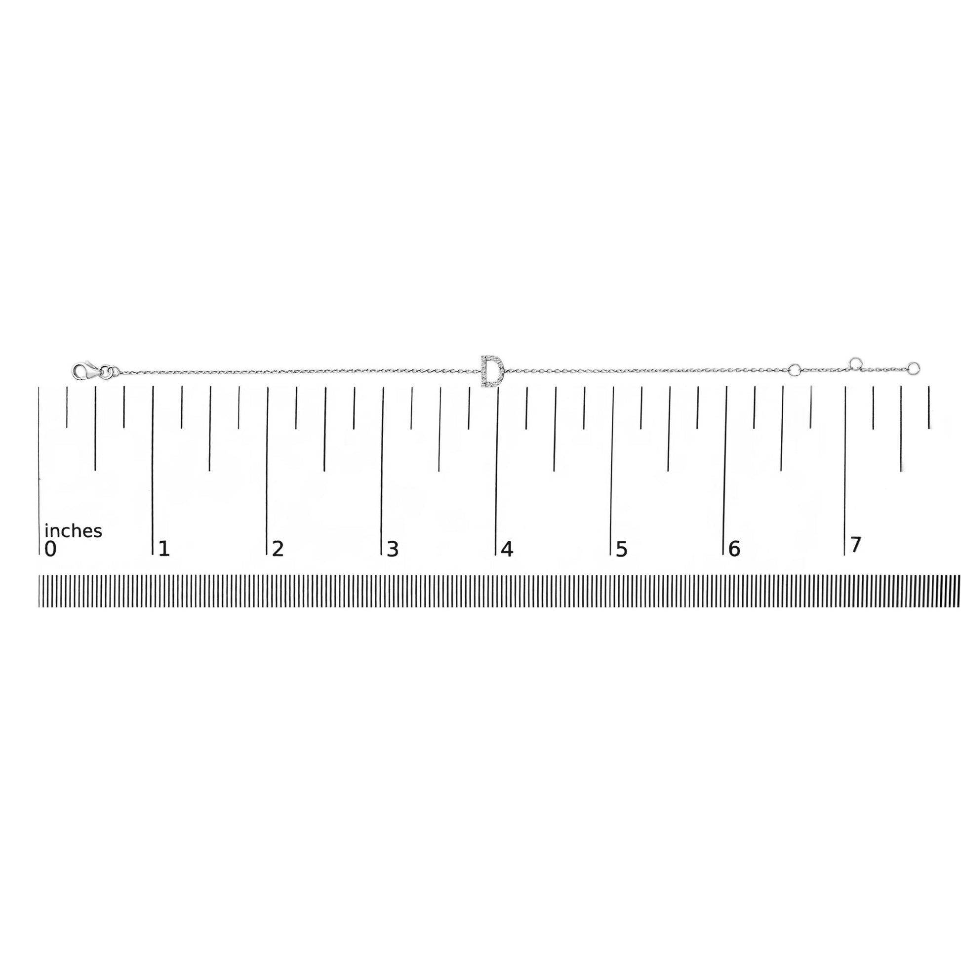 White metal bracelet with a central letter-shaped charm featuring small white gemstones in a micro-pave setting, shown laid flat on a ruler for scale from a top-down angle.