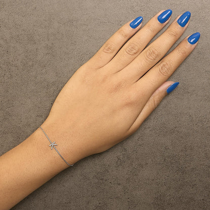 White metal bracelet with small round white gemstones in a micro-pave setting forming a letter-like shape, shown worn on a model's wrist from top angle.