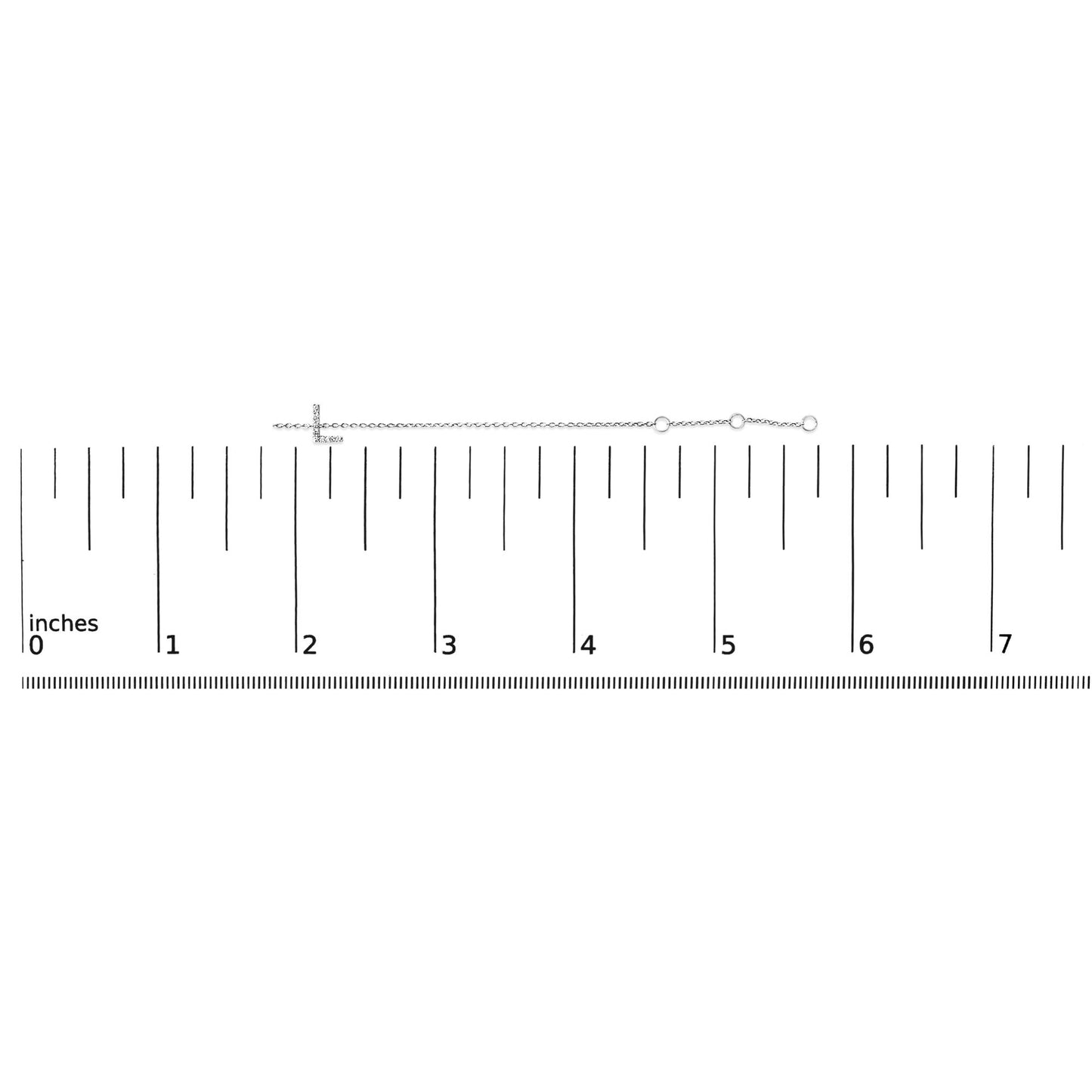 White bracelet with small round white gemstones in a micro-pave setting forming a horizontal cross, laid flat on a ruler, shot from above.
