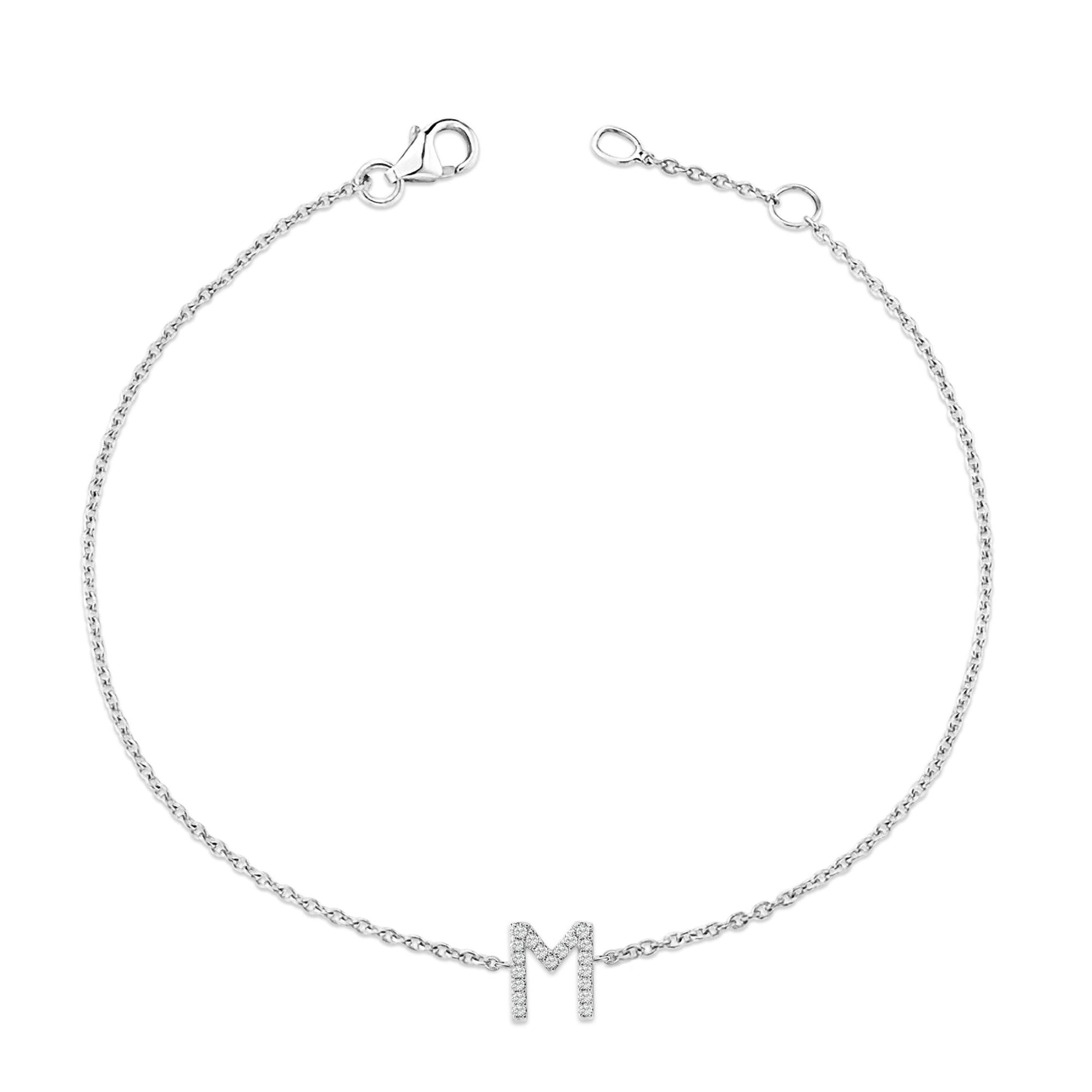White bracelet with a chain and a letter M pendant set with small white round gemstones, shown from above on a white background.