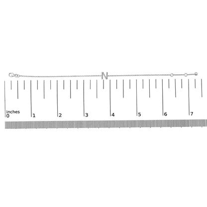 White metal bracelet with an 'N' letter centerpiece adorned with small white gemstones in a micro-pave setting, laid flat on a horizontal ruler, top-down angle.