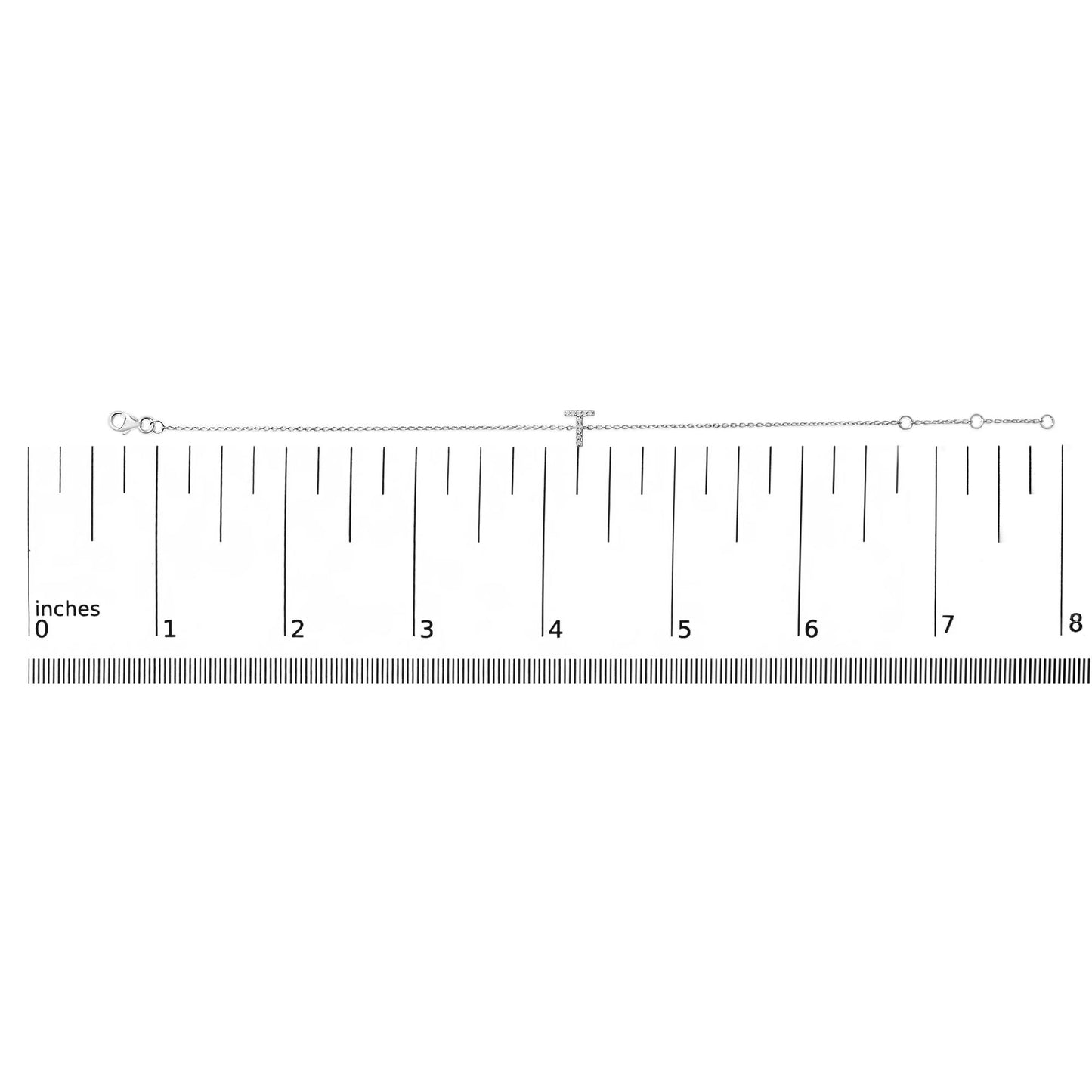 White metal bracelet with a T-shaped centerpiece set with white round gemstones in micro-pave setting, shown lying on a ruler scale viewed from above.