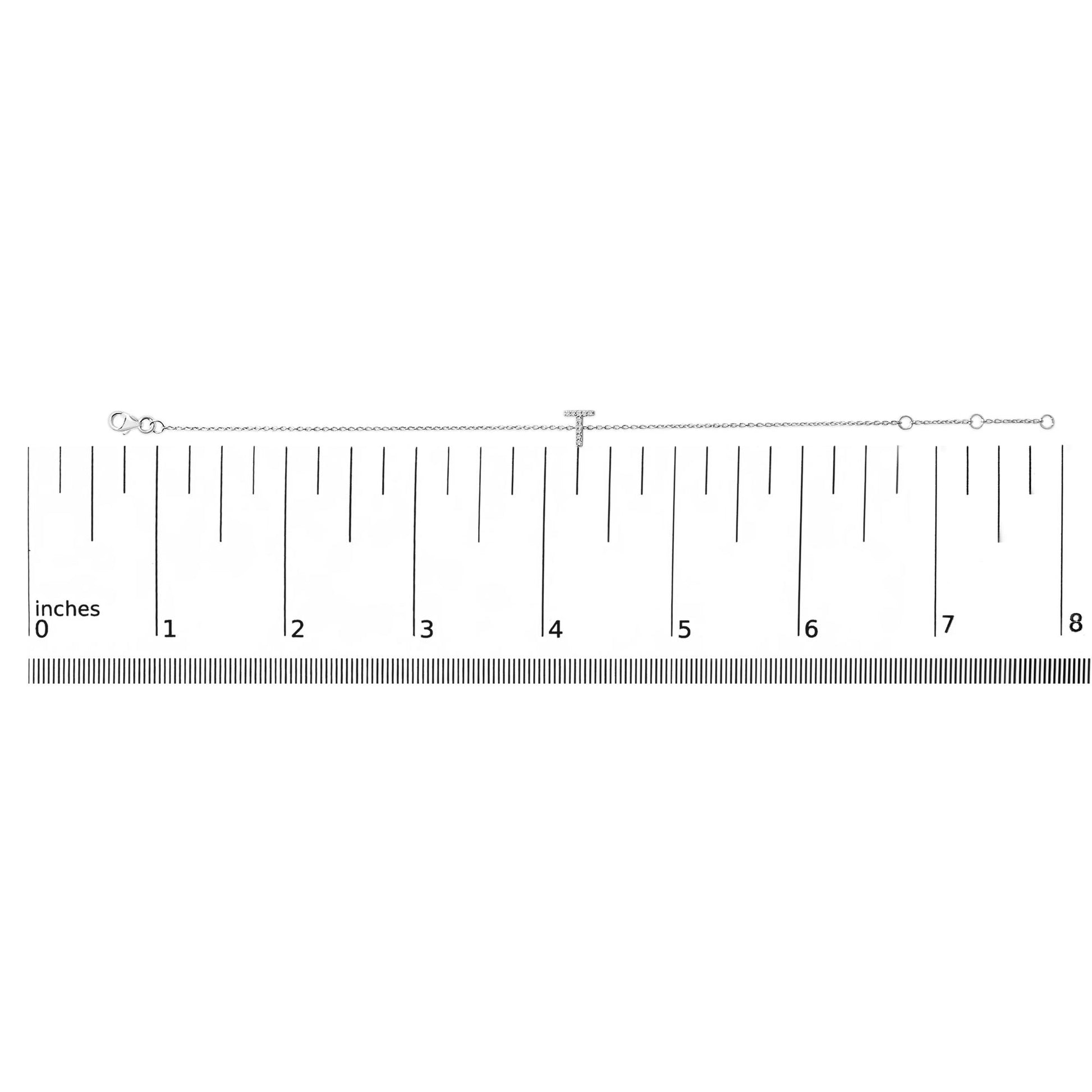 White metal bracelet with a T-shaped centerpiece set with white round gemstones in micro-pave setting, shown lying on a ruler scale viewed from above.