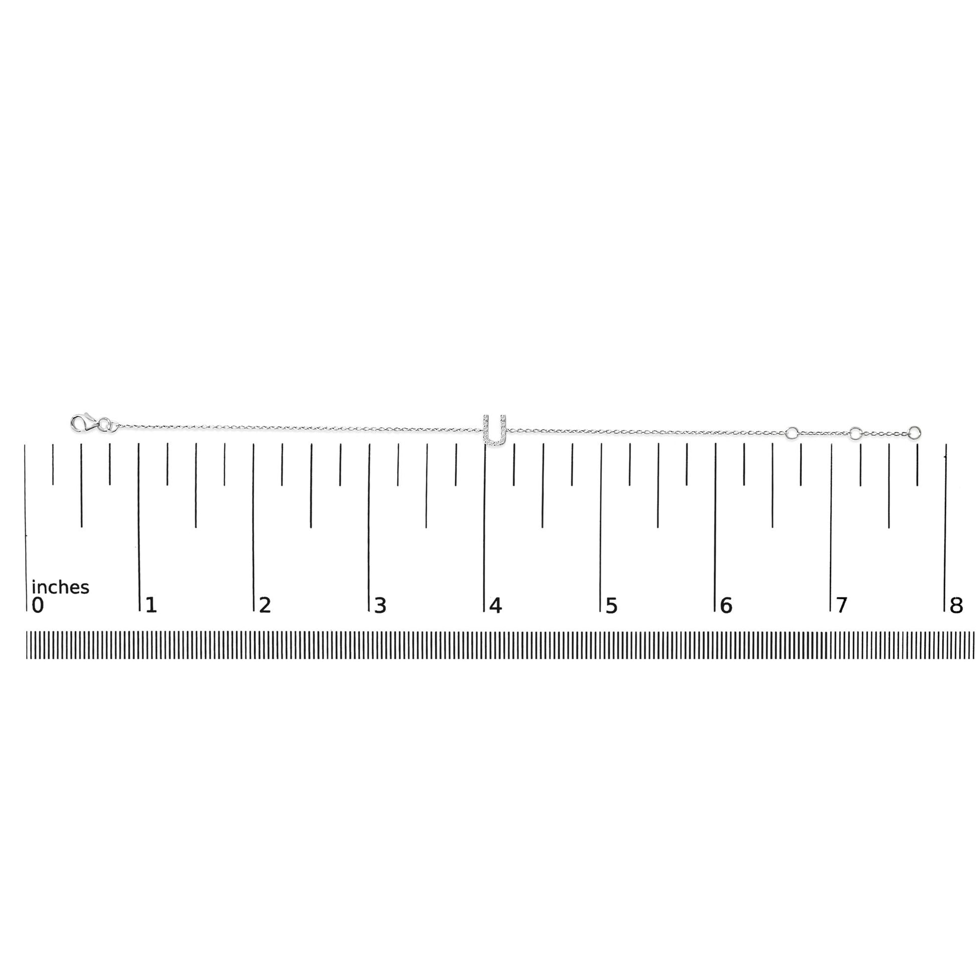 White bracelet with a central U-shaped charm set with white round gemstones in a micro-pave setting, shown on a ruler scale from a top-down angle.