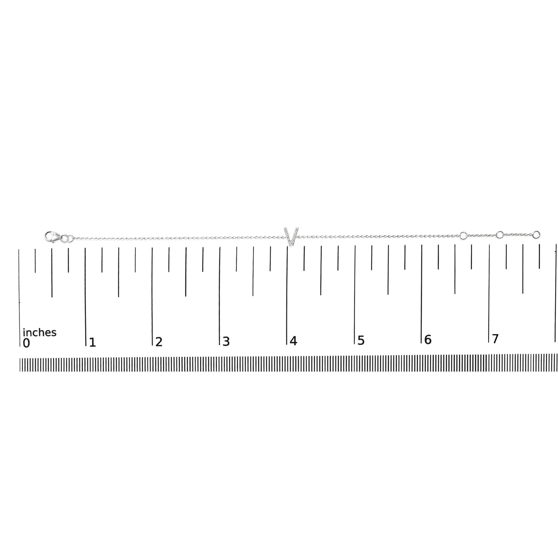 White metal bracelet with a central 'V' shape adorned with small white gemstones in a micro-pave setting, shown on a ruler scale from a top-down angle.