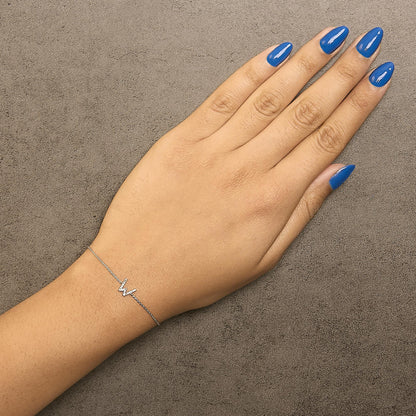 Close-up front view of a model’s hand wearing a delicate white metal bracelet with a zigzag-shaped centerpiece featuring small white gemstones in a micro-pave setting.