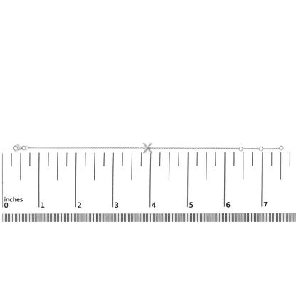 White bracelet with a chain and an X-shaped centerpiece featuring small white gemstones in a micro-pave setting, shown flat on a ruler for scale, viewed from above.