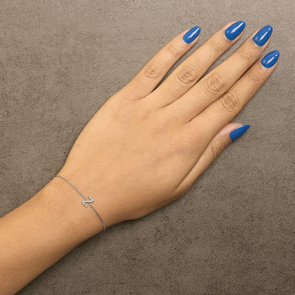 Delicate white bracelet with a zigzag-shaped centerpiece set with round white gemstones in micro-pave setting, shown worn on a model's wrist from above.