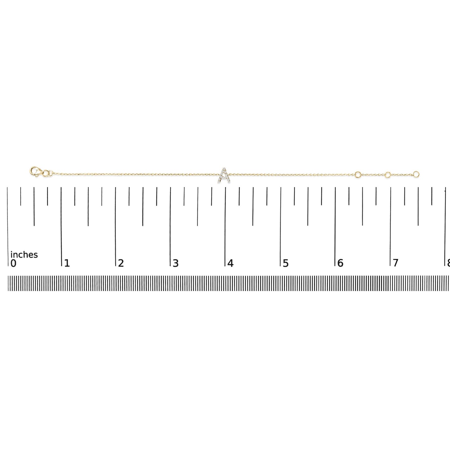 Yellow metal bracelet with a small 'A' shaped charm set with white gemstones in micro-pave setting, displayed horizontally on a ruler scale, top-down view.