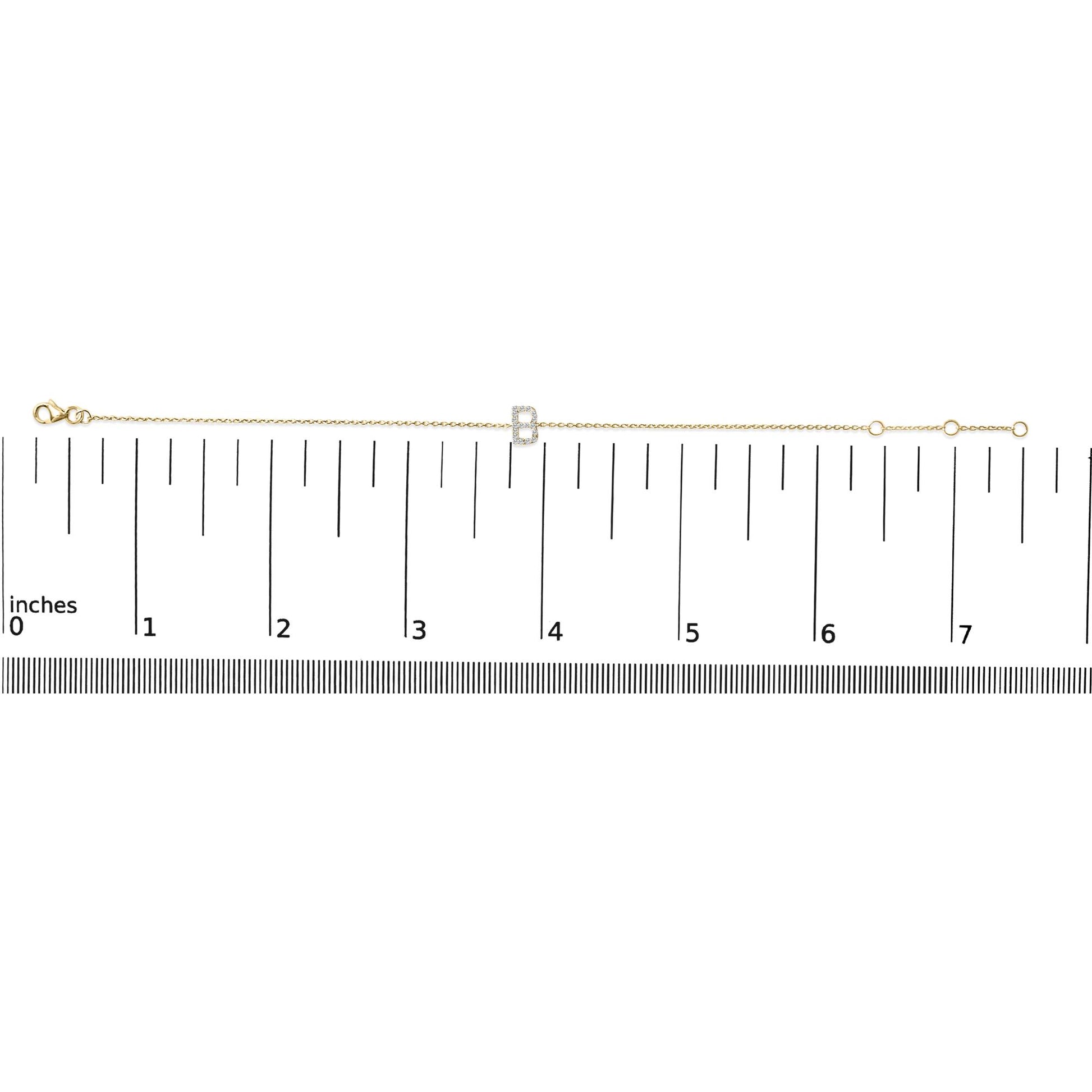 Yellow metal bracelet with a central letter-shaped charm adorned with round white gemstones in a micro-pave setting, shown on a ruler for scale from a top-down angle.