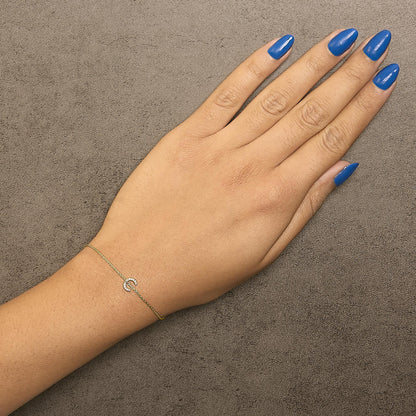 Yellow bracelet with a small horseshoe-shaped charm set with white round gemstones in a micro-pave setting, shown worn on a model's wrist from top view.