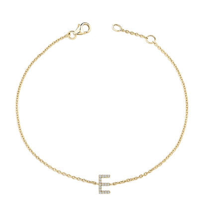 Close-up top view of a delicate yellow metal bracelet with a chain and an 'E' shaped charm adorned with white round gemstones in a micro-pave setting.